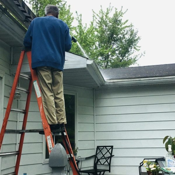 Man on ladder cleaning gutters on roof
